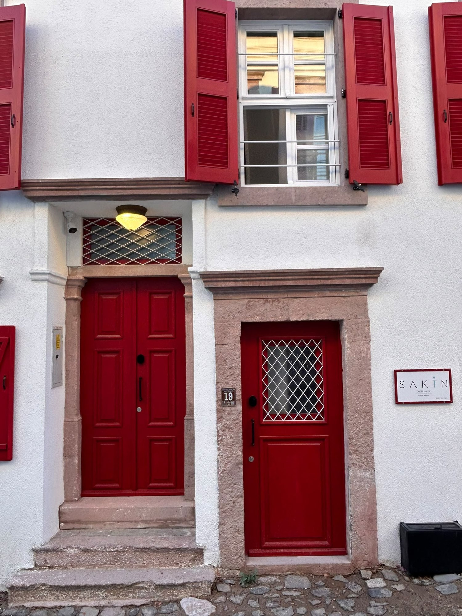 Sakin Guest House cephesi, kırmızı kapılar ve tabela, Cunda